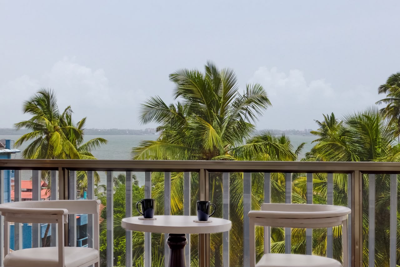 A balcony table with two mugs, overlooking palms and the bay at Dona Paula